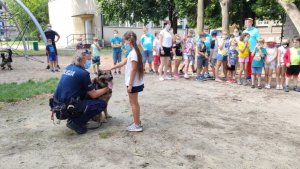 policjant z psem służbowym kuca przed dziewczynką, która głaszcze psa Kaira