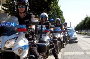 czterech policjantów na motocyklach służbowych w drugiej alei przodem do fotografującego