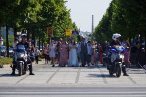 dwóch policjantów na motocyklach stoją po dwóch stronach grupy pielgrzymów, idących po pasach