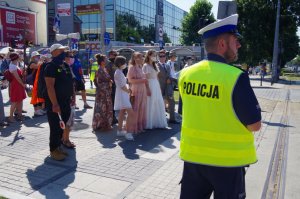 policjant ruchu drogowego w białej czapce i gwizdkiem kieruje ruchem, pielgrzymi przechodzą po przejściu dla pieszych