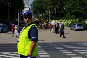 policjant ruchu drogowego w białej czapce i gwizdkiem kieruje ruchem, pielgrzymi przechodzą po przejściu dla pieszych