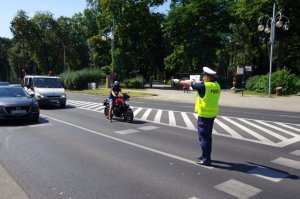 policjant przed przejściem dla pieszych kieruje ruchem - pokazuje sygnały kierującym