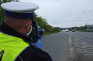 głowa policjanta fotografowana od tyłu jak patrzy w ekran radaru i mierzy prędkość przejeżdżających trasą samochodów