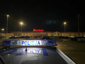 napis policja podświetlony na radiowozie, w tle parking Auchan