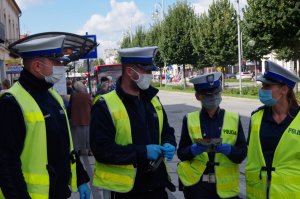 dwóch policjantów i dwie policjantki z ruchu drogowego w białych czapkach rozmawiają ze sobą w alejach w tle autobus MPK