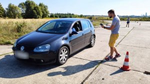 instruktor stoi na płycie lotniska i rozmawia z kierowcą siedzącym w samochodzie osobowym