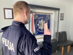 nowo przyjęty policjant stoi w mundurze tyłem do fotografującego, składa ślubowanie przodem do Sztandaru Komendy Miejskiej Policji w Częstochowie