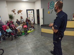 Policjant z prewencji stoi przez grupa podopiecznych fundacji i opowiada o pracy w policji