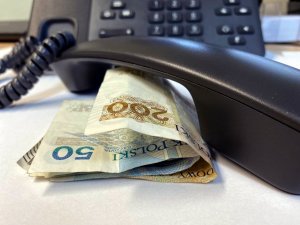 słuchawka telefonu leży na stoliku przy niej banknoty pieniędzy, w tle telefon z klawiaturą