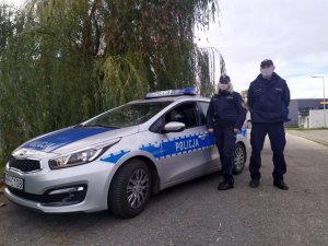 policjantka i policjant w mundurach stoją przy radiowozie i pozują do zdjęcia