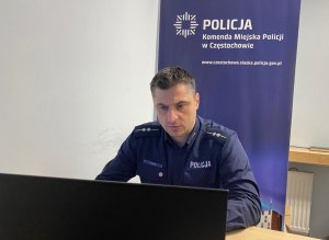 policjant siedzi przed komputerem, za nim z tyłu rollup z napisem Komenda Miejska Policji w Częstochowie