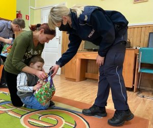 Policjantka wręcza paczkę dziecku które trzyma opiekunka.