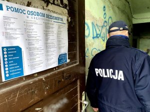 policjant wchodzi do budynku, w tle widać na drzwiach wejściowych plakat o bezdomności