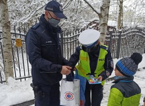 policjanci rozdają uczestnikom spotkania kolorowanki i odblaski