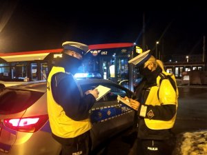 policjantka i policjant stoją przy radiowozie, w tle autobus MPK