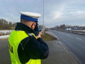 policjant trzyma ręczny miernik prędkości przy twarzy i dokonuje pomiaru prędkości w rejonie przejścia dla pieszych