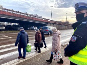 policjant stoi przed przejściem dla pieszych i patrzy w kierunku nadjeżdżających samochodów