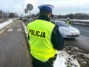 policjant stoi tyłem, patrzy w kierunku drugiego policjanta, wykonującego kontrole pojazdu