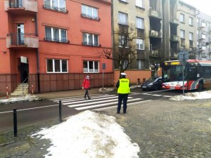 policjantka przy przejściu dla pieszych po przejściu przechodzi piesza w czerwonej kurtce