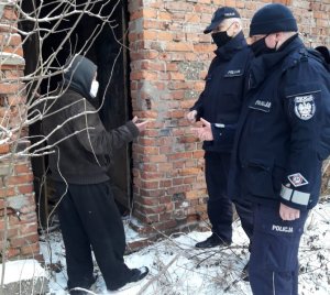 umundurowani policjanci stoją przed opuszczonym budynkiem i rozmawiają z napotkanym tam bezdomnym