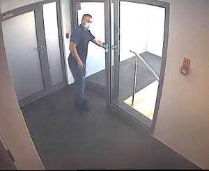 mężczyzna ubrany w spodnie jeansowe i niebieską koszulę z krótkim rękawem otwiera drzwi prowadzące na klatkę schodową