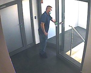 mężczyzna ubrany w spodnie jeansowe i niebieską koszulę z krótkim rękawem otwiera drzwi prowadzące na klatkę schodową