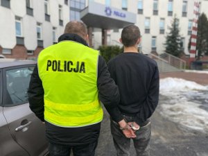 zatrzymany mężczyzna prowadzony jest przez nieumundurowanego policjanta w kamizelce odblaskowej przed głównym wejściem do Komendy Miejskiej Policji w Częstochowie.