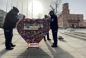 umundurowani policjanci na Placu Biegańskiego wrzucają plastikowe nakrętki do czerwonego metalowego serca