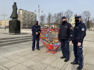 policjanci pozują przy wypełnionym nakrętkami metanowym sercu, w tle pomnik Marszałka Piłsudskiego