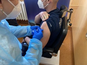 pielęgniarka podaje dawkę szczepionki w zastrzyku w ramię policjanta siedzącego w fotelu