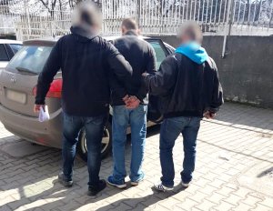 zatrzymany mężczyzna jest prowadzony przez nieumundurowanych policjantów na parkingu