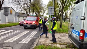 policjant z ruchu drogowego stoi przy drodze z podniesiona ręką. W ręce trzyma tarczę do zatrzymywania pojazdów.