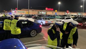 policyjny radiowóz i policjanci na pierwszym planie, w tle samochody zaparkowane na parkingu pod centrum handlowym