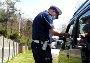 policjant przekazuje dokumenty kierowcy siedzącemu w samochodzie