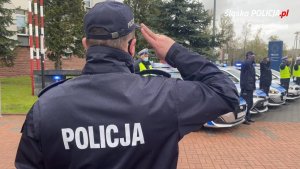 policjant salutuje, w tle policjanci i radiowozy policyjne