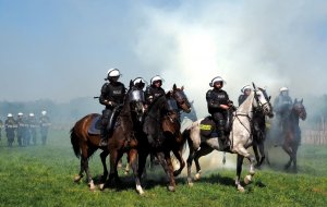 policjanci na koniach służbowych idą w kłębach dymu