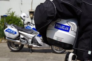 policjant w ręce trzyma kask z napisem policja, w tle motocykl policyjny