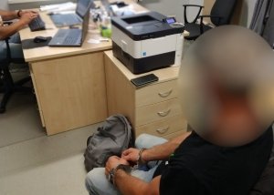 zatrzymany mężczyzna z kajdankami założonymi na ręce siedzi przed biurkiem policjanta