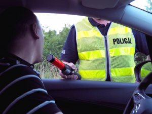 policjant w kamizelce odblaskowej sprawdza trzeźwość kierującego poprzez specjalne urządzenie