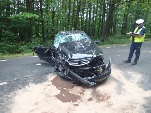 rozgnieciony samochód na jezdni obok policjant, który pisze.