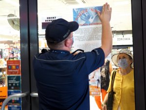 policjant rozwiesza plakaty na drzwiach wejściowych do sklepów