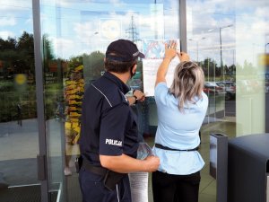 policjant rozwiesza plakaty na drzwiach wejściowych do sklepów