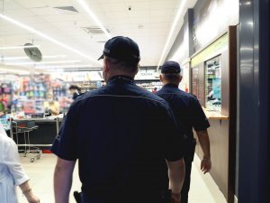 policjanci w mundurach kontrolują sklepy - spacerują alejkami sklepów z regałami, na których stoi towar