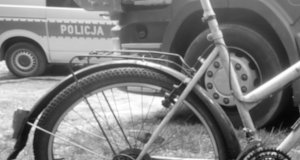 zdjęcie w kolorach czarnym i białym przedstawiające rower, a w tle radiowóz oraz karoserię pojazdu ciężarowego