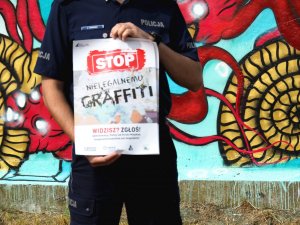 zbliżenie na ręce policjanta, który trzyma plakat promujący akcje &quot;Stop nielegalnemu graffiti&quot;