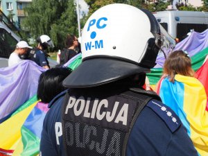 policjanci maszerują drogami miasta zabezpieczając Marsz Równości - w tle kolorowa flaga uczestników zgromadzenia