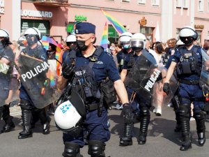 policjanci maszerują drogami miasta zabezpieczając Marsz Równości - w tle kolorowa flaga uczestników zgromadzenia