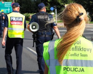 kobieta w kamizelce z napisem zespół antykonfliktowy policji, w tle policjant w kamizelce z napisem dowódca akcji