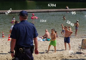 policjant stoi przodem do zbiornika wodnego na plaży - w pobliżu bawią się dzieci