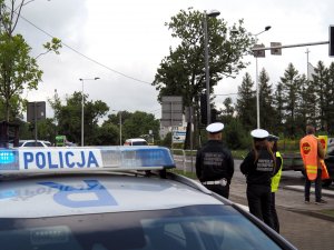 na pierwszym planie napis policja na radiowozie, w tle policjantka i funkcjonariusze Inspekcji Transportu Drogowego stoją przy przejściu dla pieszych